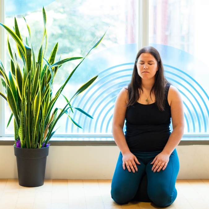 Fair skinned woman meditating deeply while sitting on comfortable knee position on floor.
