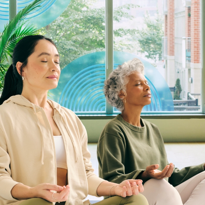 Two diverse women meditating while sitting crossed legged in a calm and soothing mindful yoga studio
