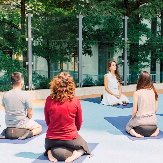 A group of diverse people meditating in sitting positions outside on yoga mats on a beautiful day