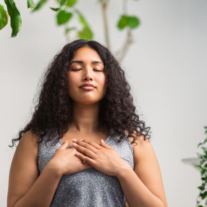 Hispanic woman with curly long hair with hands over her heart concentrating