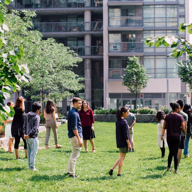 A group of diverse teachers in a circle outside examining their surroundings